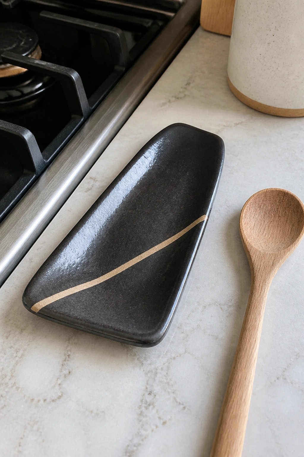 Black ceramic dish with gold line beside wooden spoon on marble countertop
