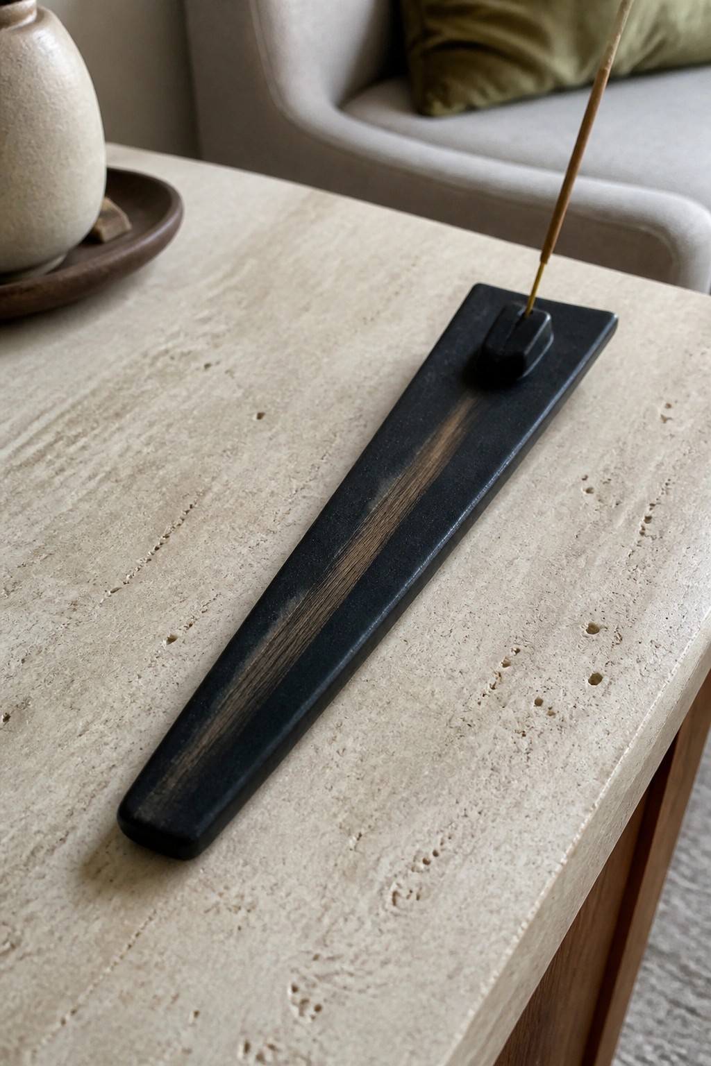 Black incense holder with burning stick and ash streak on stone table.