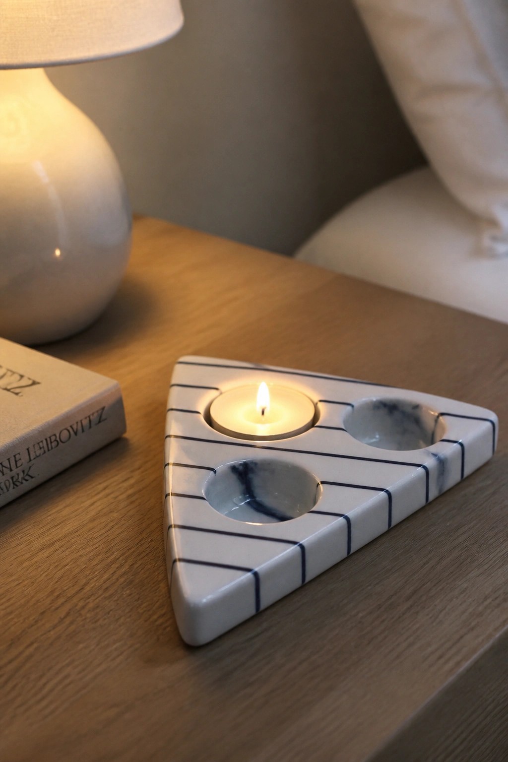 Triangular white marble candle holder with black stripes and lit tealight on wood table