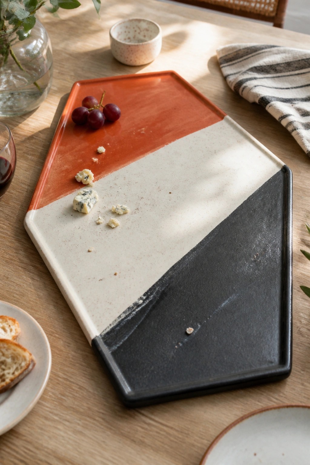 Geometric ceramic tray in orange, white, and black with grapes and blue cheese
