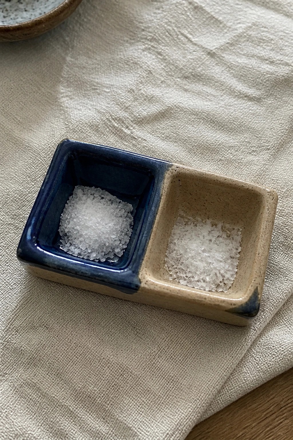 Divided ceramic dish with blue and beige compartments holding white salt on linen fabric