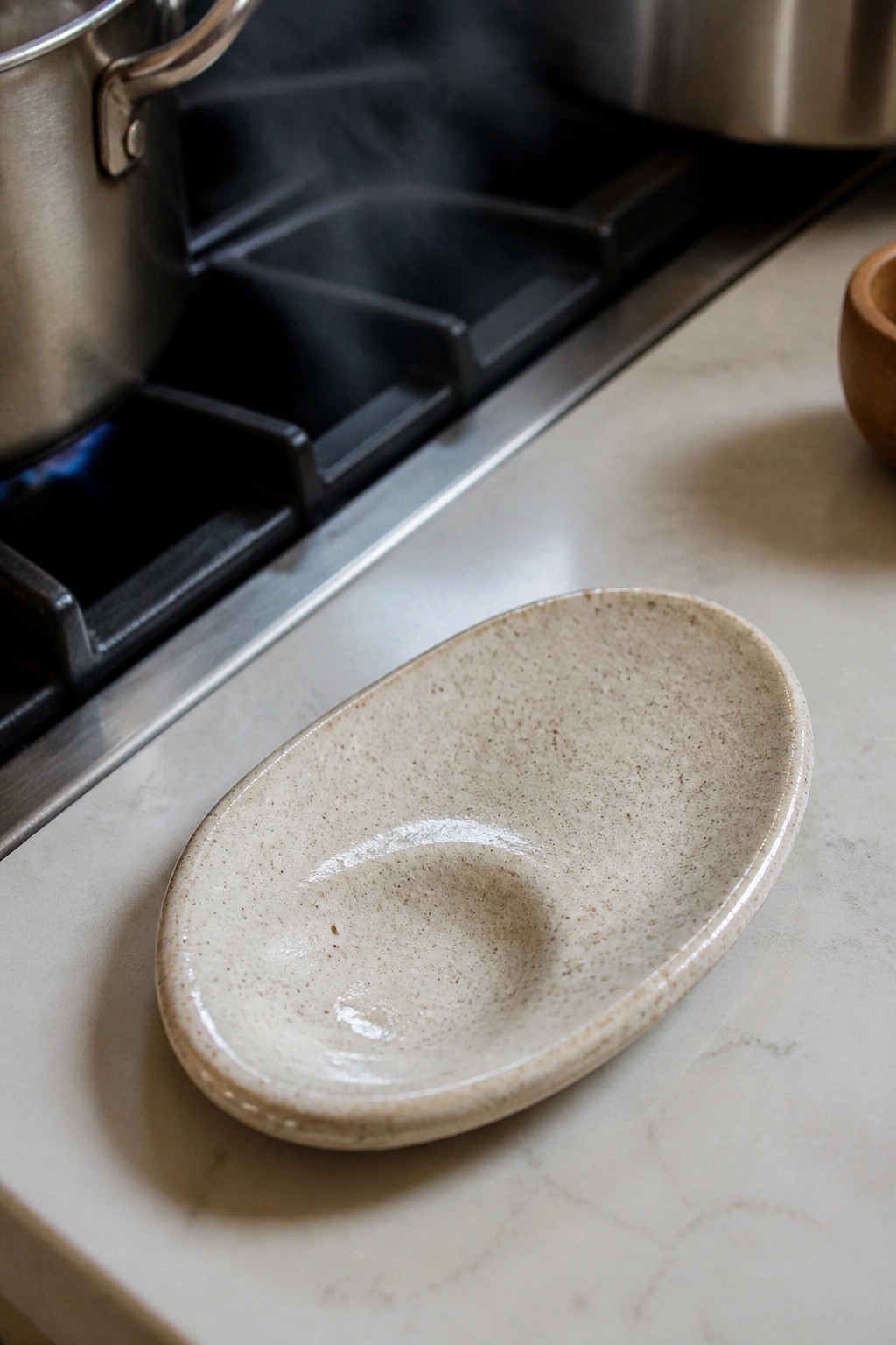 Speckled beige ceramic bowl on marble countertop near lit gas stove.