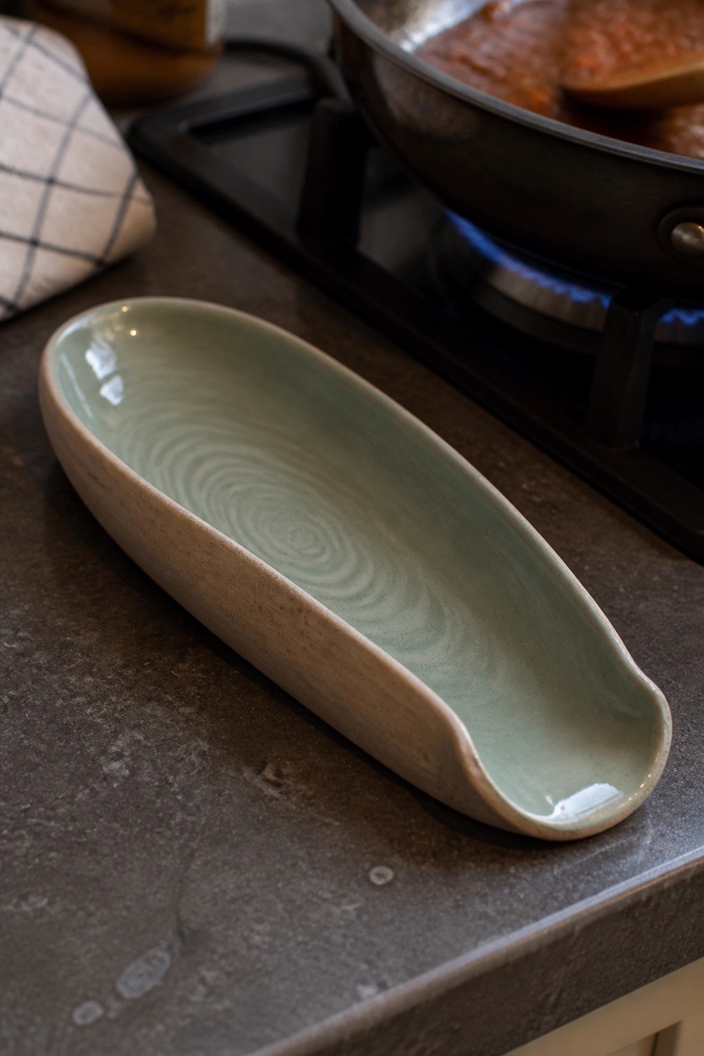 Elongated green ceramic dish on dark counter near pan of red sauce on stove