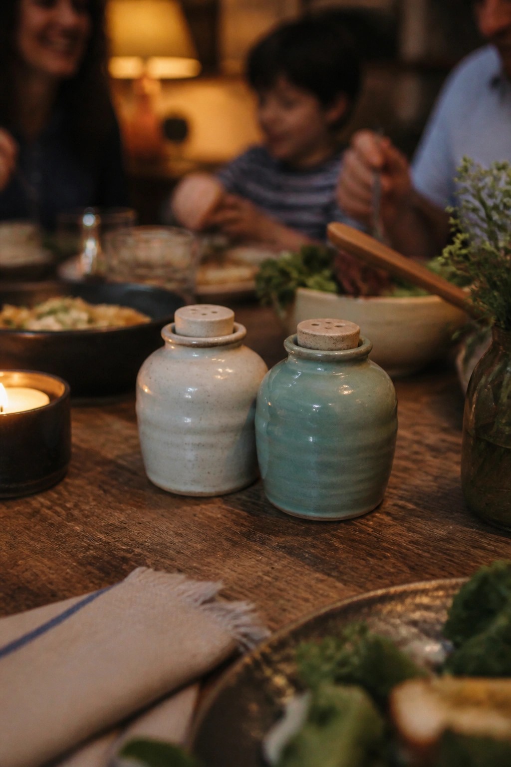Wooden dinner table with turquoise salt shakers, lit candle, and blurred family eating