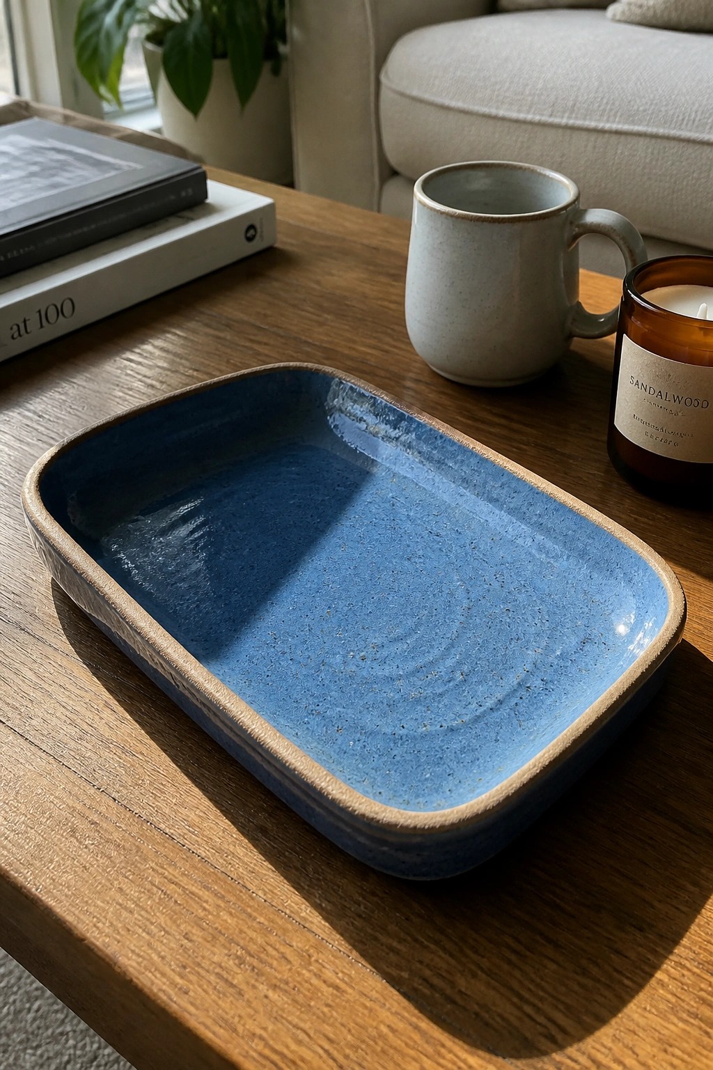 Blue ceramic tray on wooden table beside mug, candle, and books
