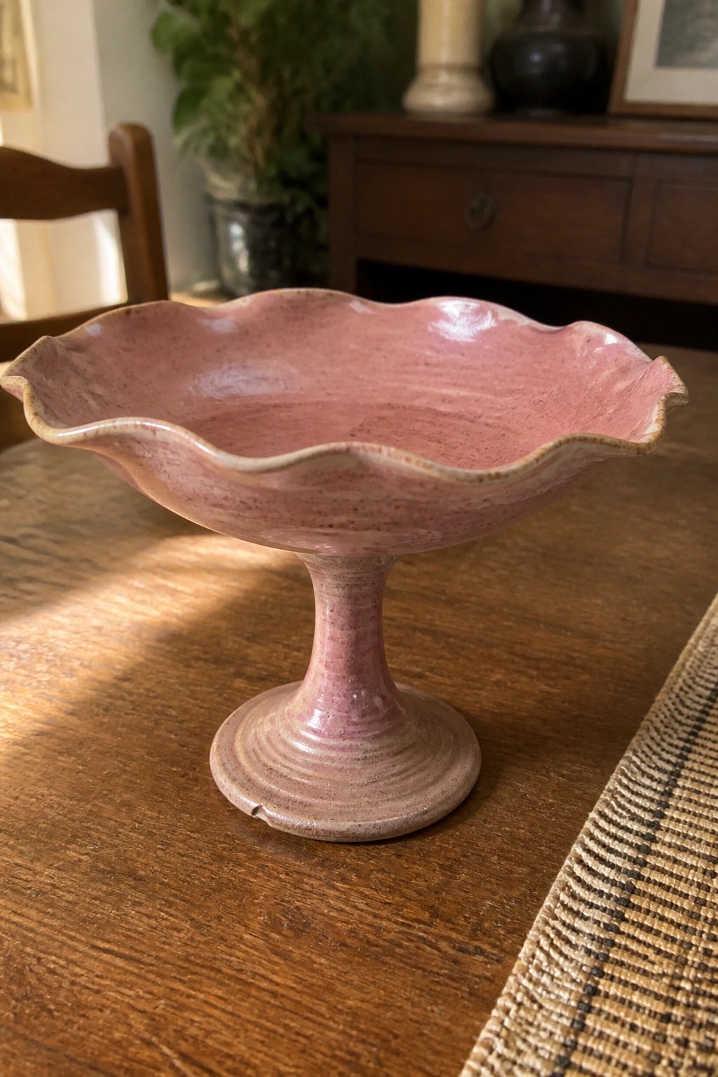 Pink ceramic pedestal bowl with scalloped rim on wooden table
