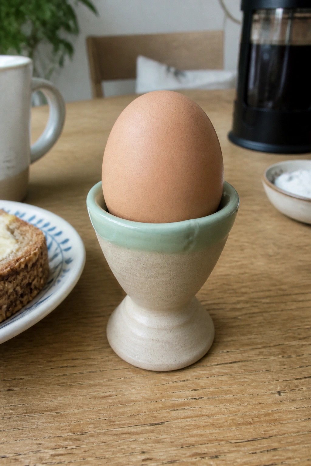 Brown egg in a beige ceramic cup with light green rim on wooden table.
