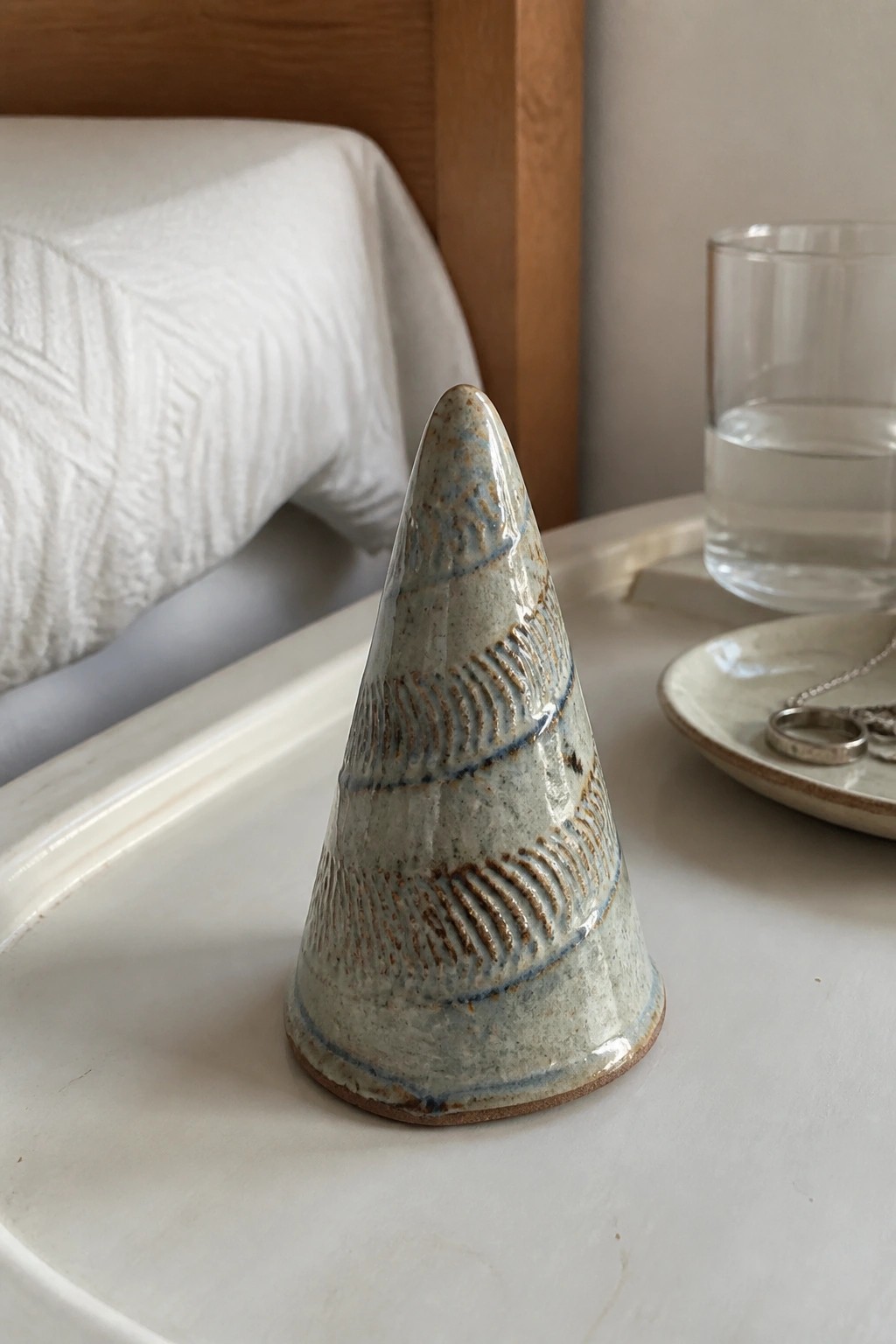 Ceramic cone with blue-brown patterns on white tray beside water glass and jewelry