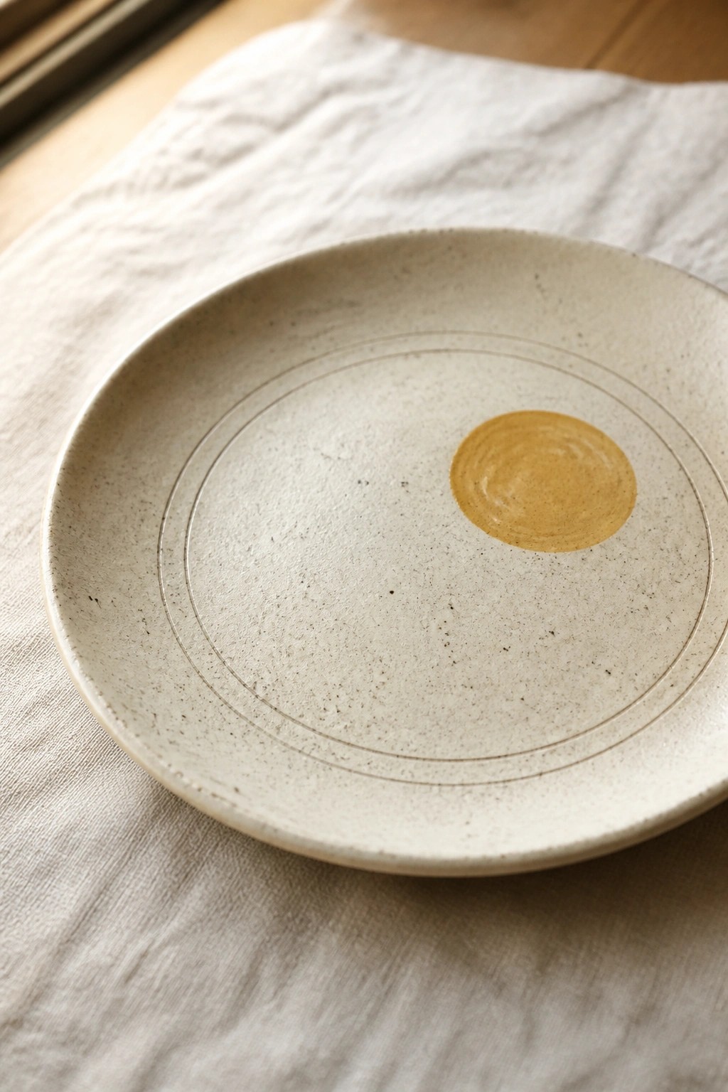 Speckled ceramic plate with concentric circles and yellow swirl on white cloth