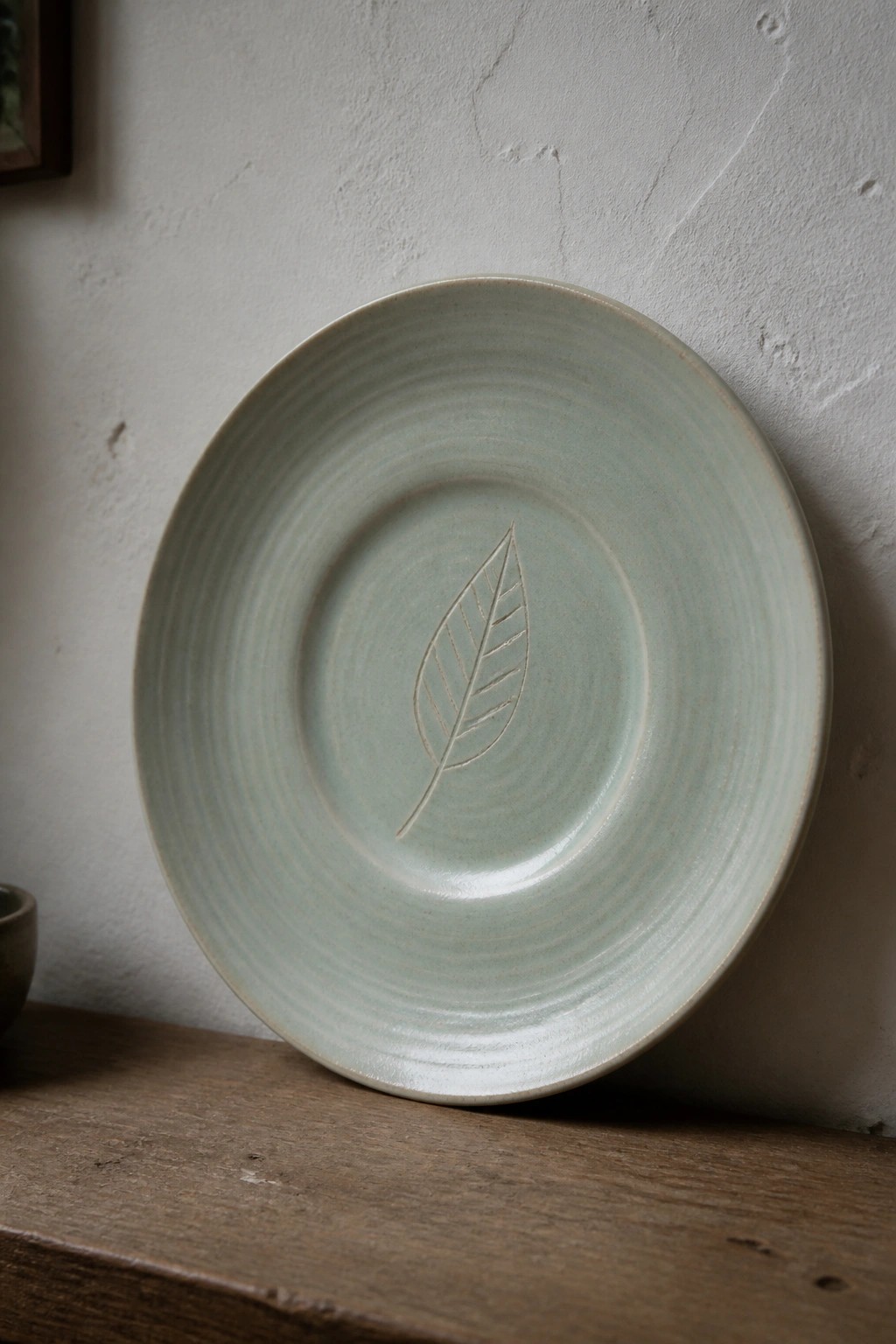 Pale green ceramic plate with central leaf design on wooden surface