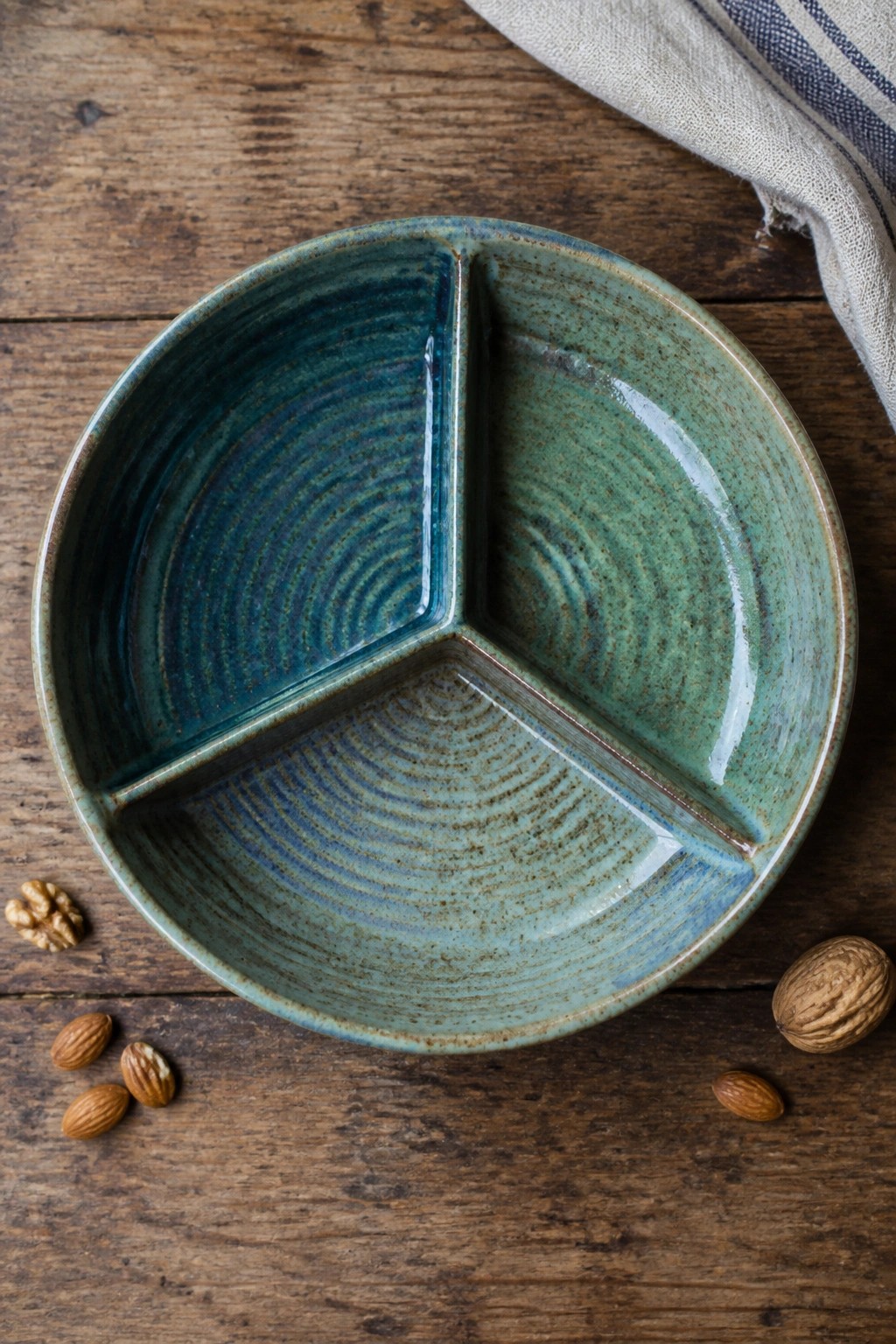 Blue-green three-section ceramic bowl on wood with almonds and walnuts nearby