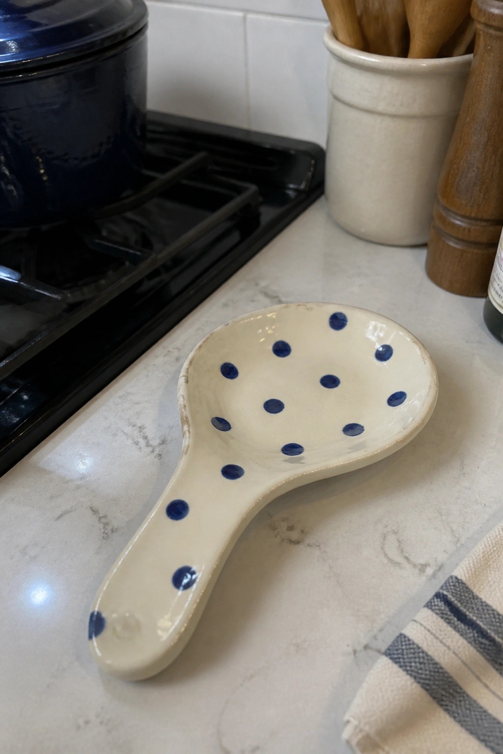 White ceramic spoon rest with blue polka dots on marble kitchen counter