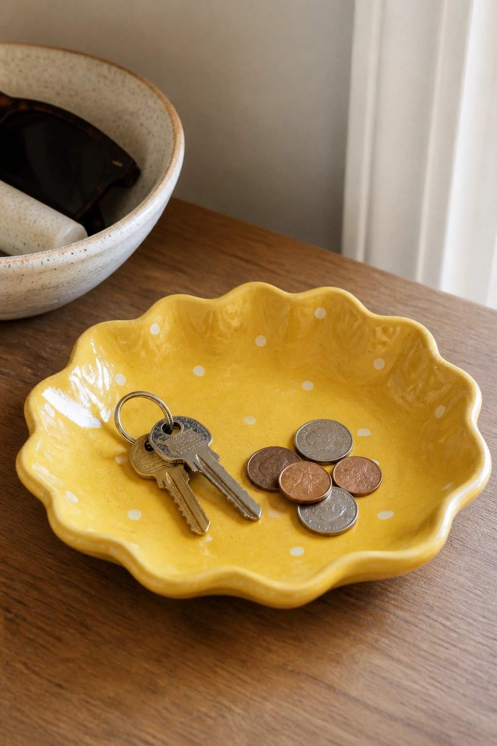 Yellow scalloped bowl with white dots holding keys and coins on wood