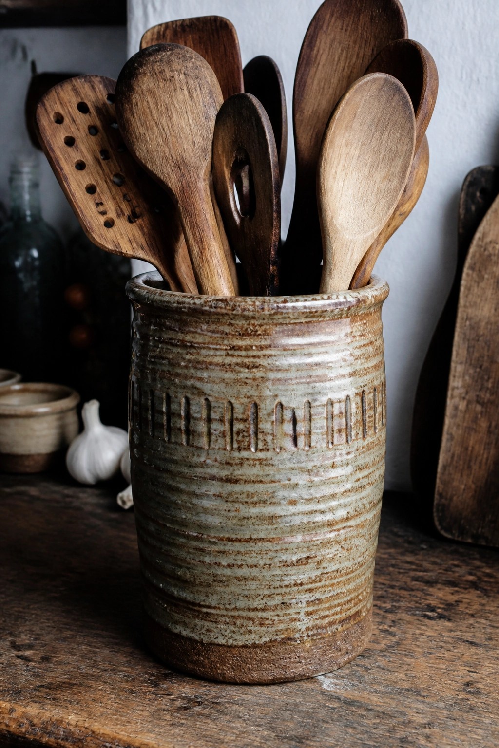 Rustic ceramic crock filled with assorted wooden spoons and kitchen utensils on table
