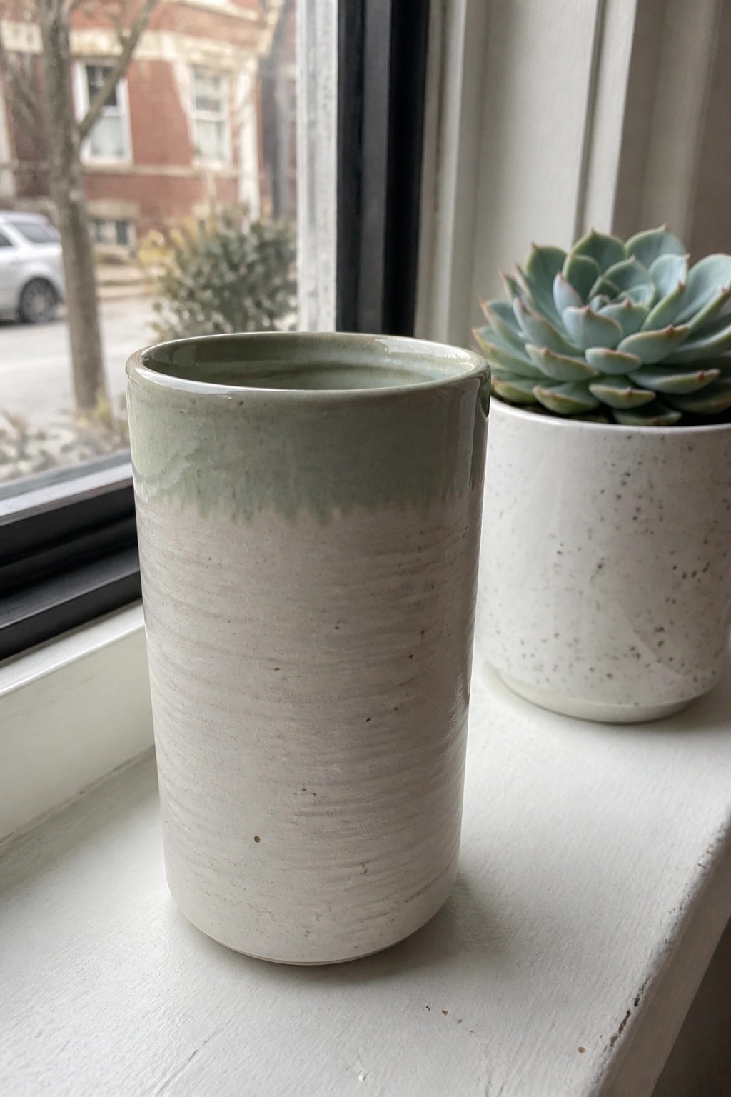 Ceramic cup with green rim beside succulent in white pot on windowsill