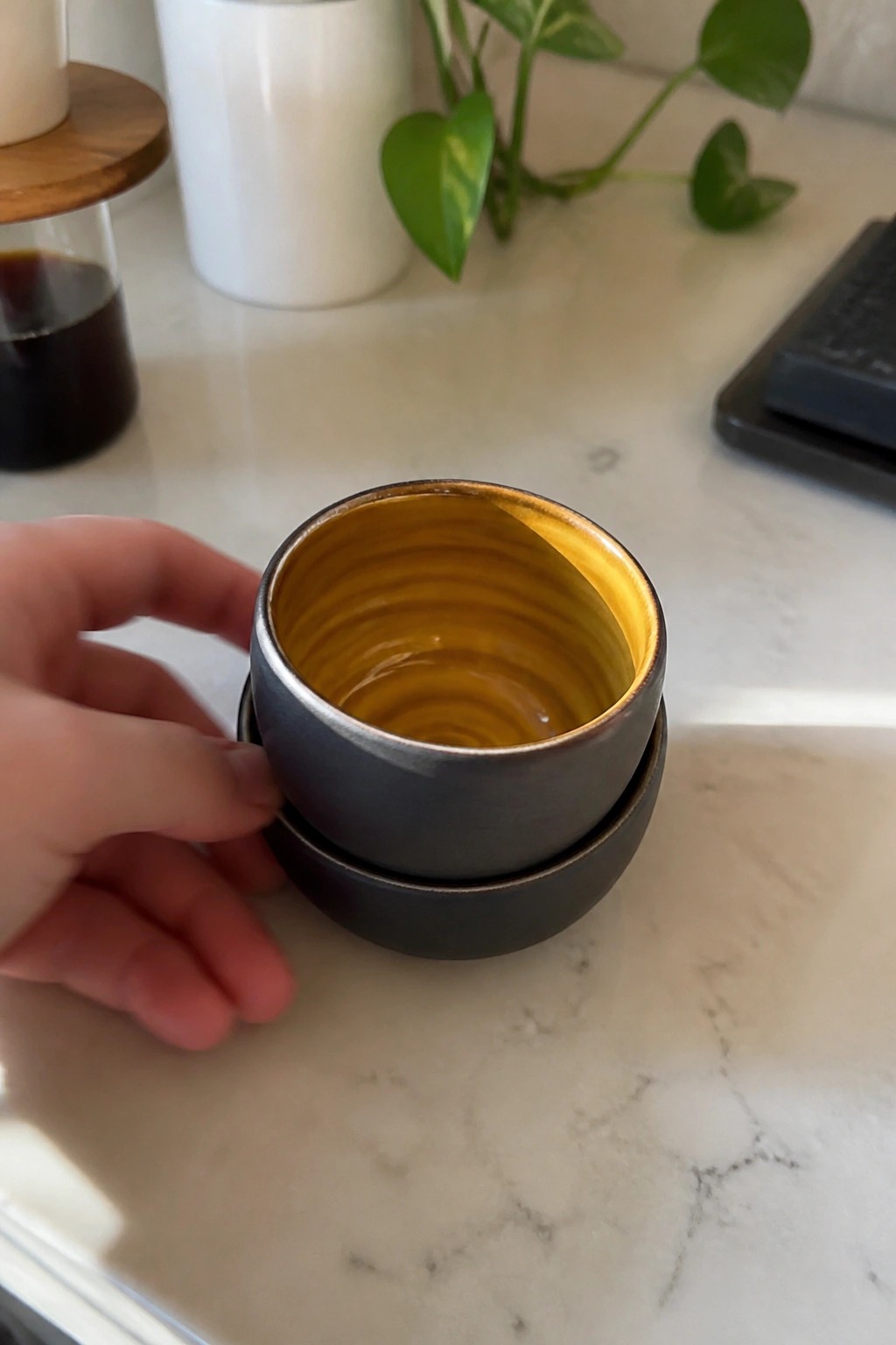 Hand holding stacked black bowls with glossy yellow ridged interior on marble counter