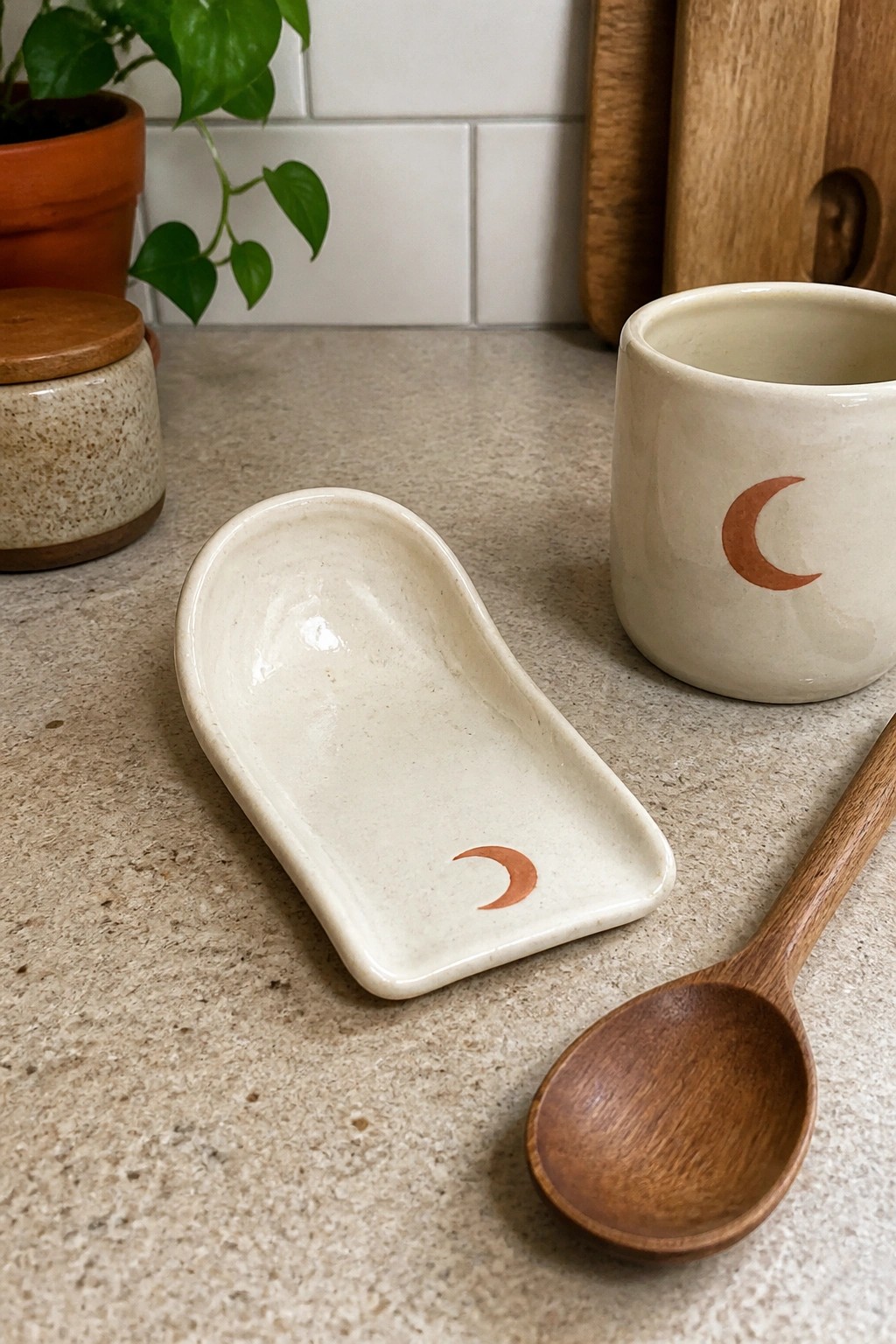 Ceramic spoon rest and mug with orange crescent moons beside wooden spoon on counter
