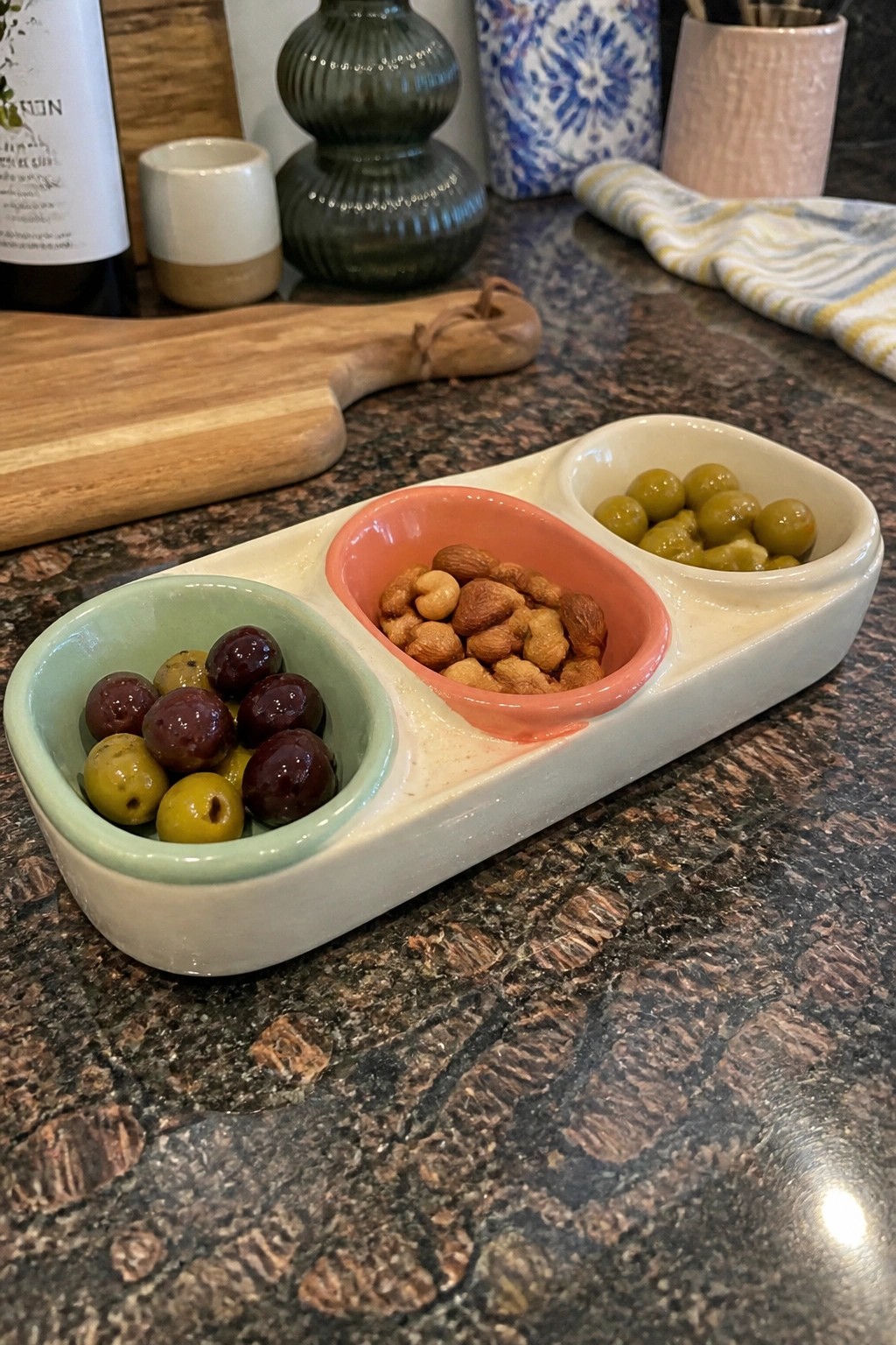 Colorful ceramic divided tray with olives and mixed nuts on marble counter