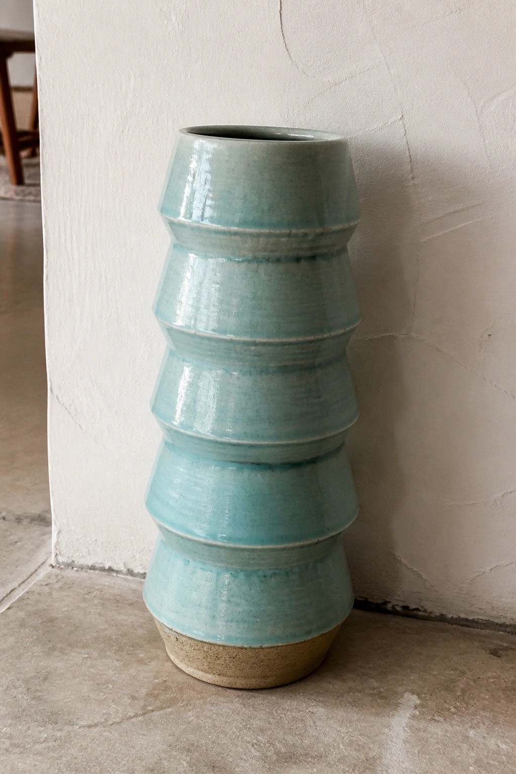 Tall turquoise ceramic vase with stacked rings and unglazed base on concrete floor