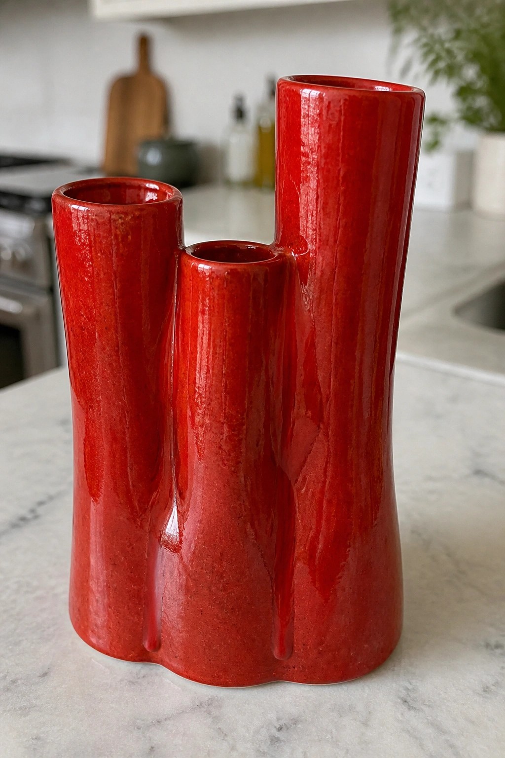 Red glossy ceramic triple vase with three openings on marble kitchen counter