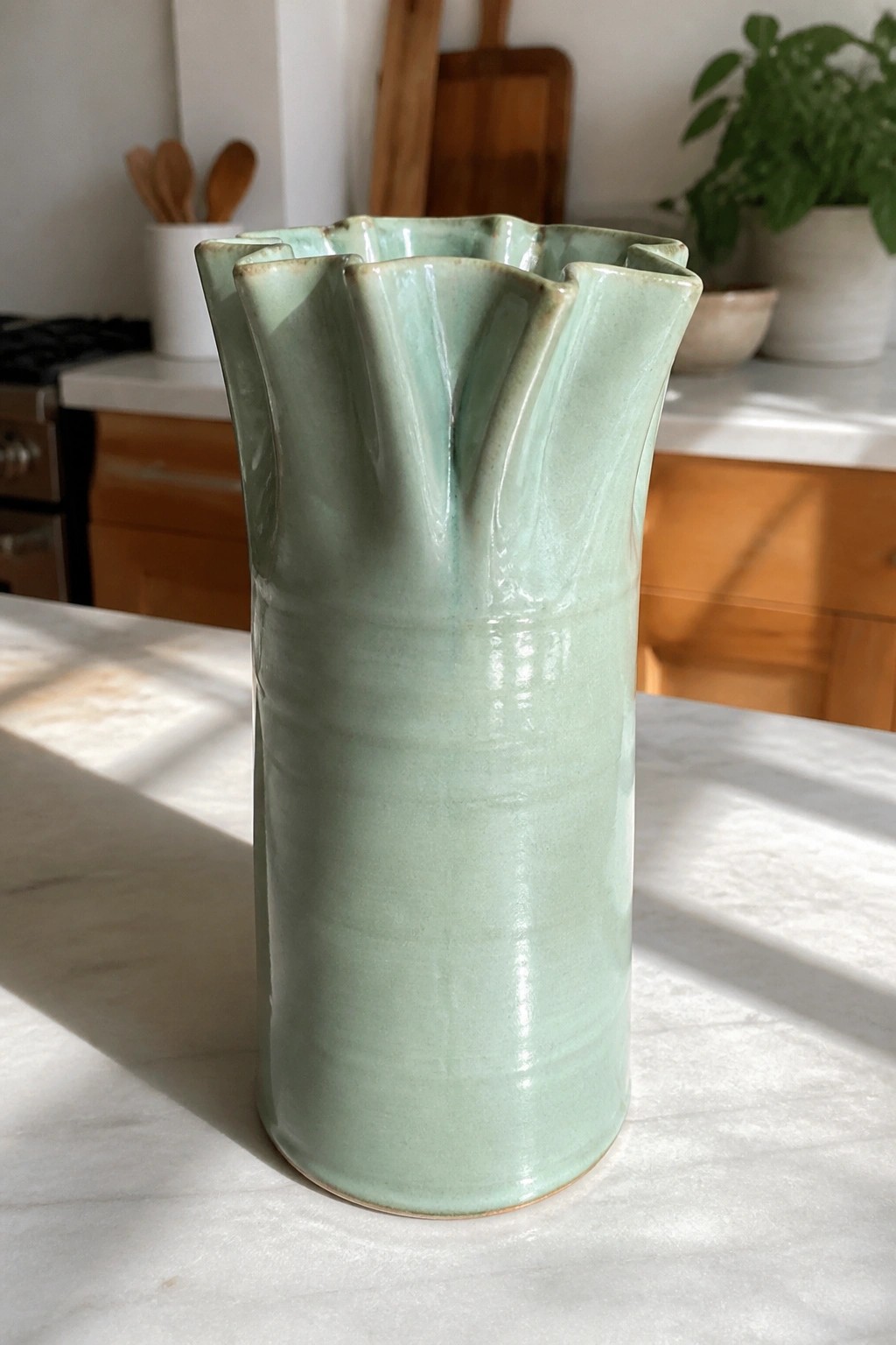 Mint green ceramic vase with scalloped rim on marble kitchen counter