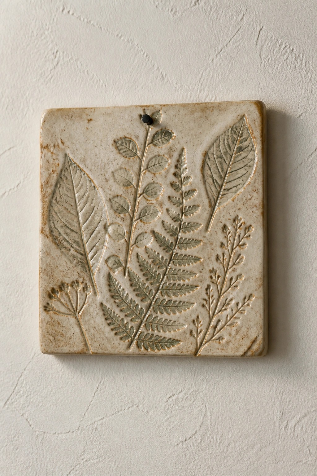 Square ceramic tile with embossed fern and leaf patterns on white wall