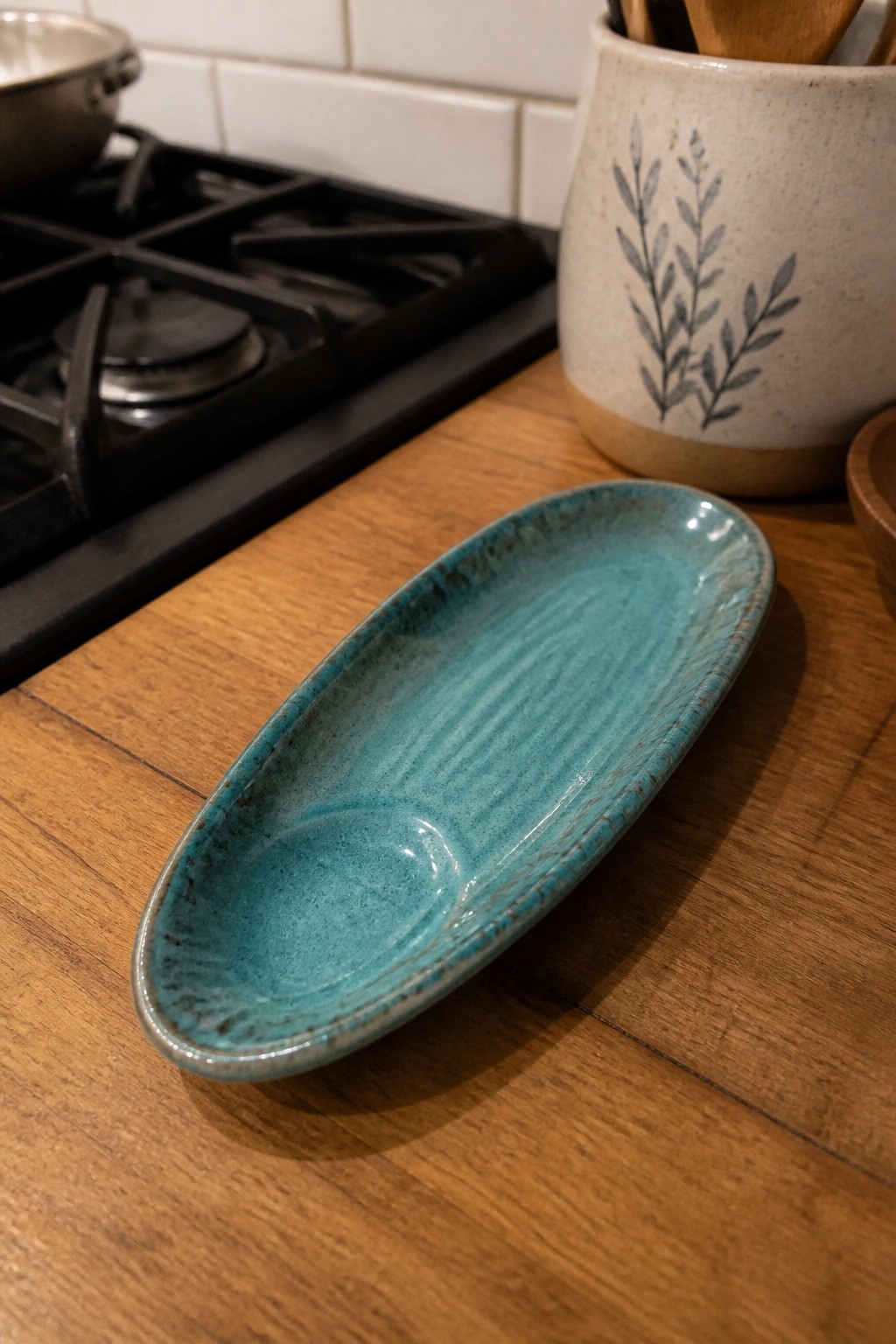 Turquoise glazed ceramic oval dish on wooden kitchen counter with stovetop behind.