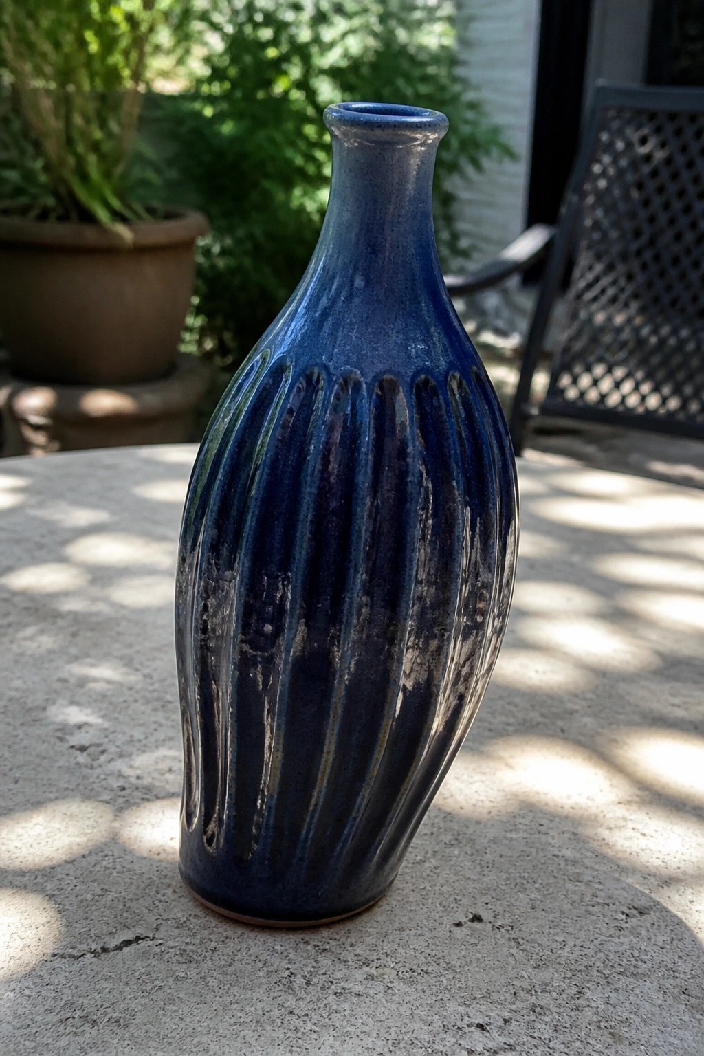 Blue glazed ceramic vase with fluted sides on sunlit concrete table.