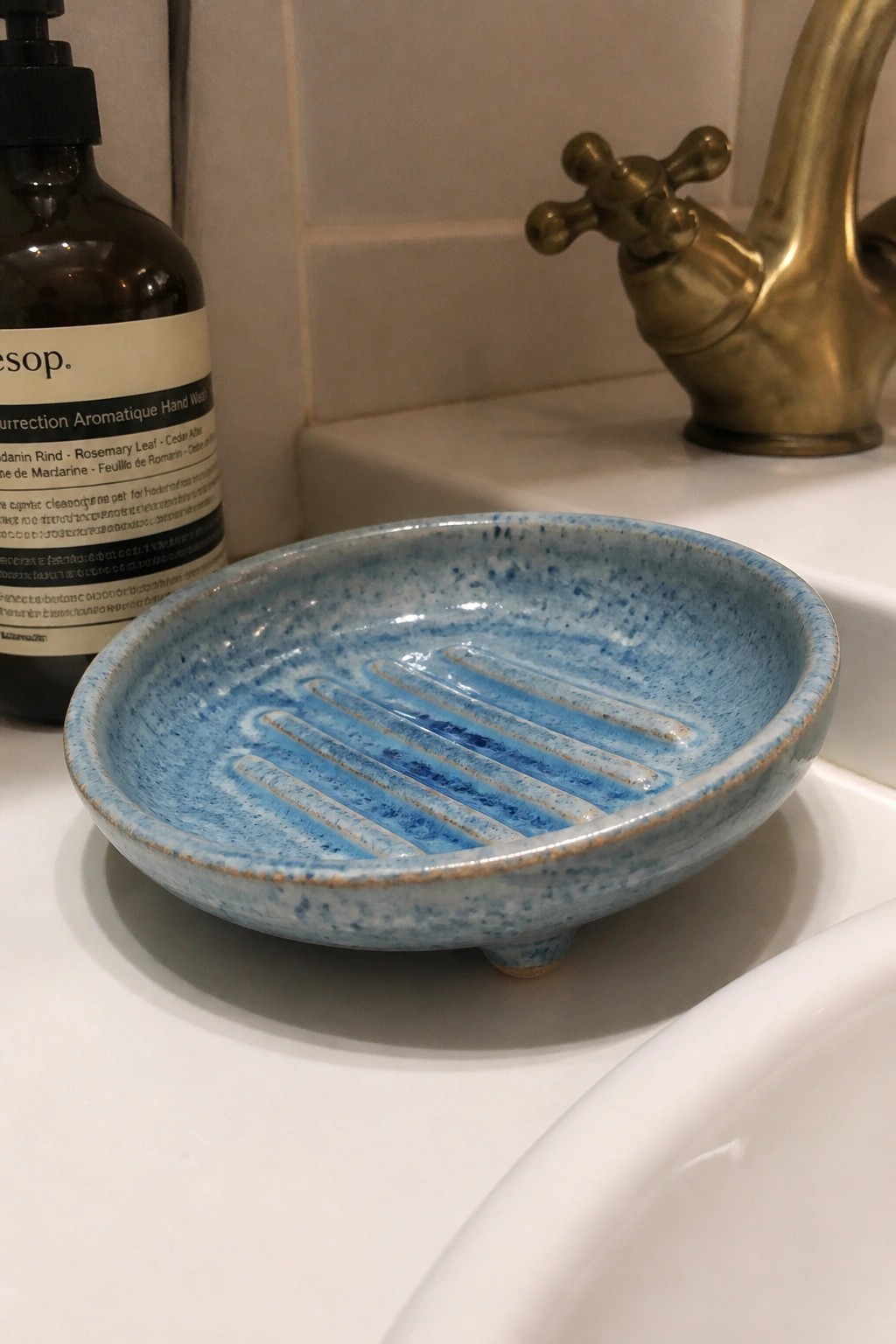 Blue speckled soap dish with ridges on white sink near brass faucet