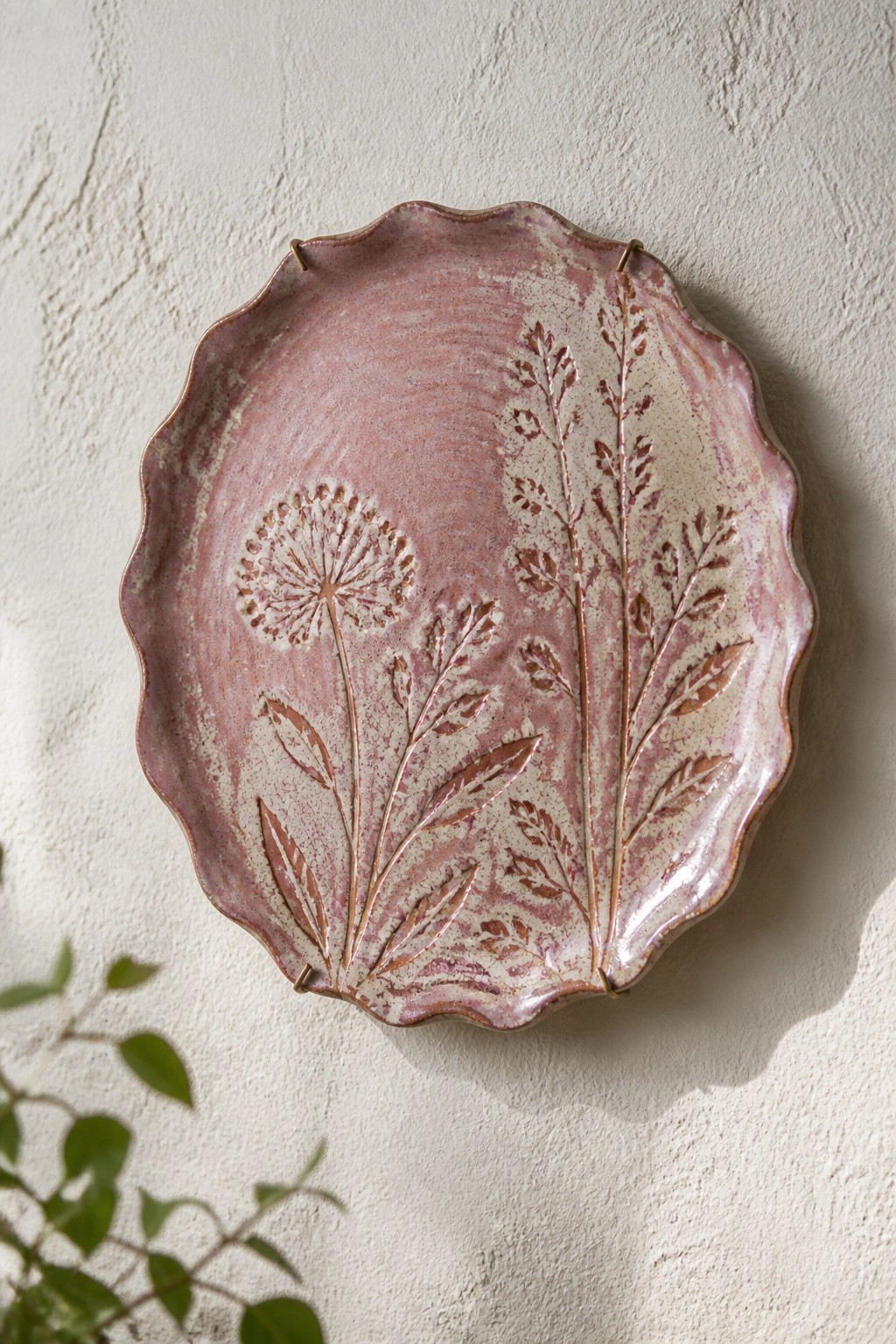 Pink scalloped ceramic platter with embossed dandelions mounted on white wall