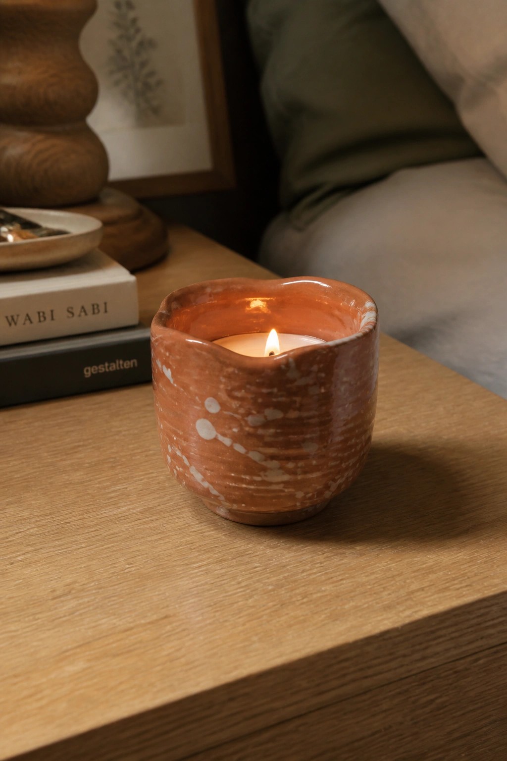 Lit candle in a speckled reddish ceramic holder with wavy rim on wood