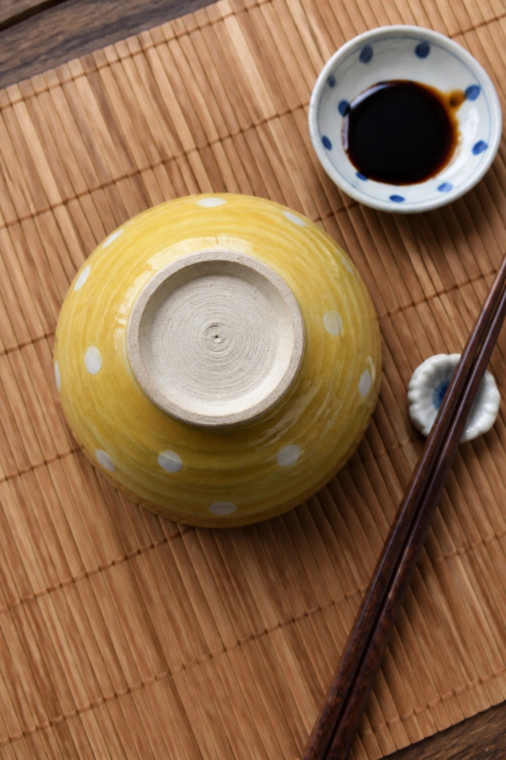 Yellow polka-dot bowl upside down near soy sauce and chopsticks on bamboo mat