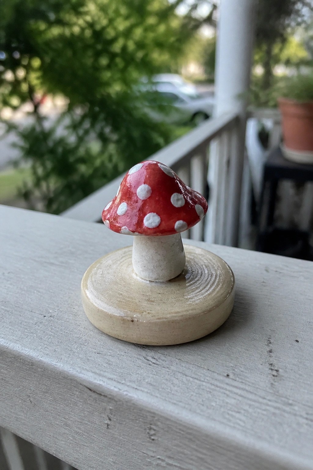 Red mushroom with white spots on beige base atop gray wooden railing