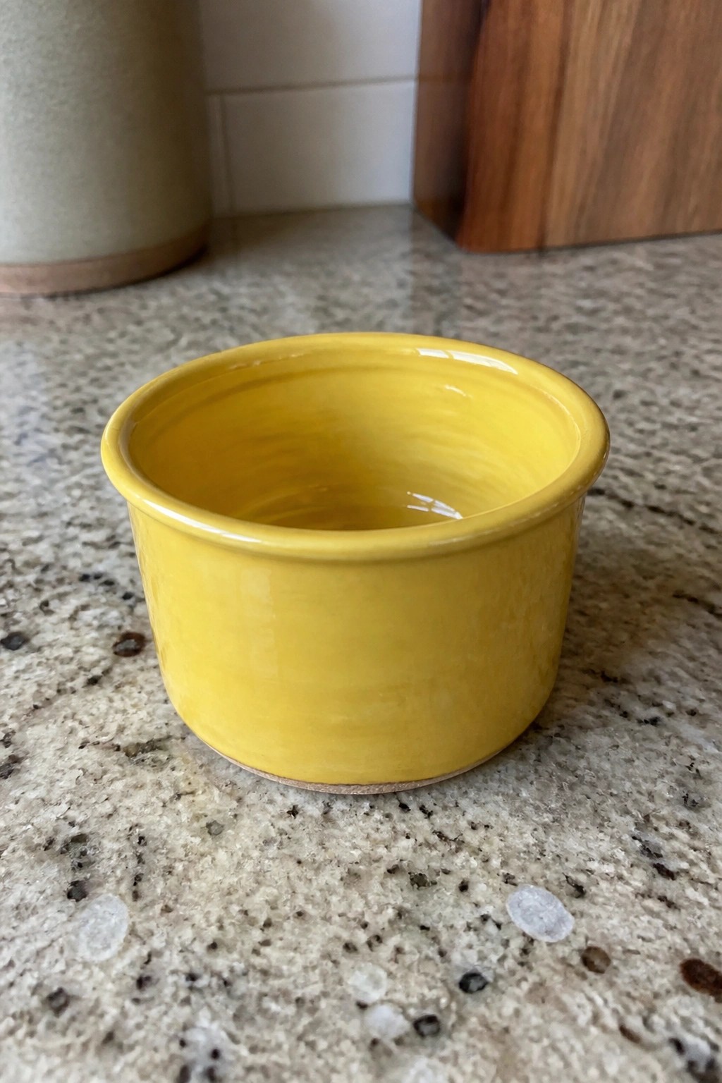 Yellow ceramic bowl on speckled granite countertop with wooden board in background.