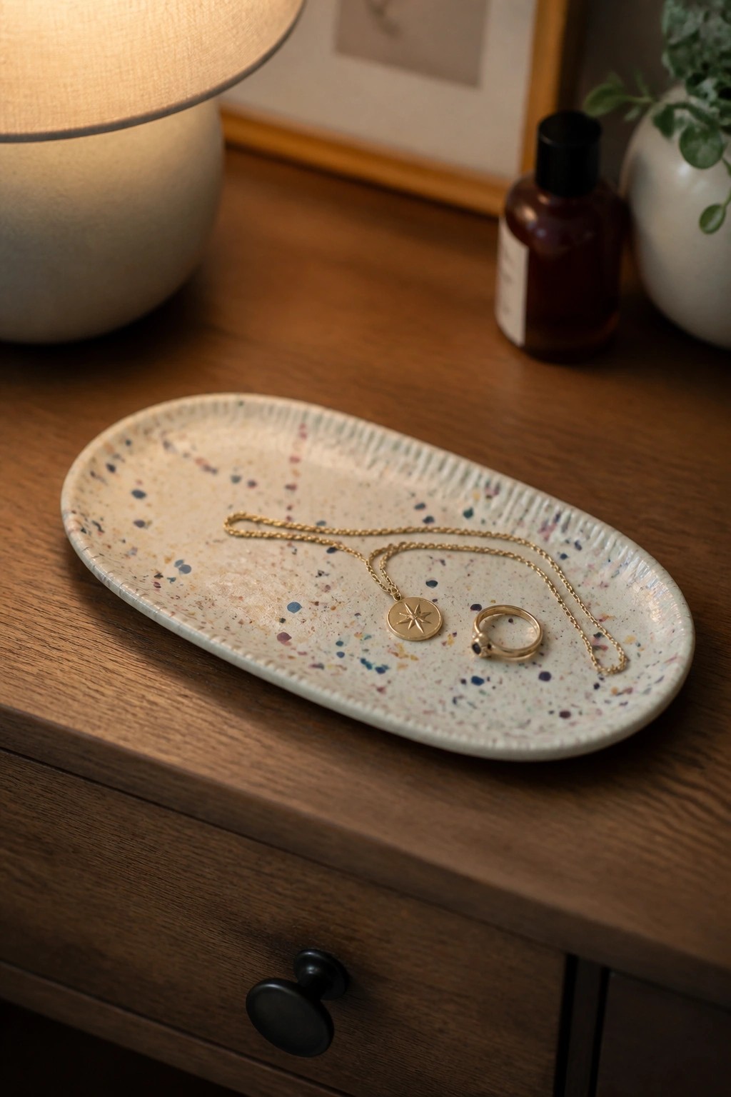 Speckled oval ceramic tray with jewelry on a wooden dresser.