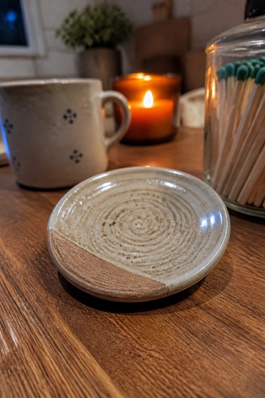 Small ceramic plate with spiral glaze on wooden table near lit candle and mug