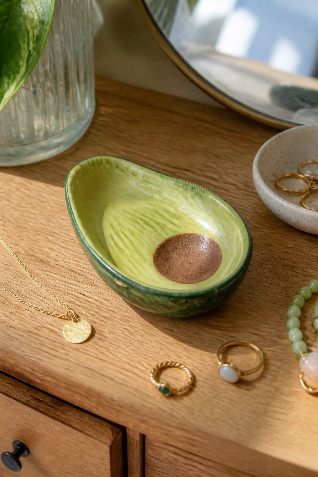 Avocado-shaped ceramic bowl with gold jewelry on wooden dresser
