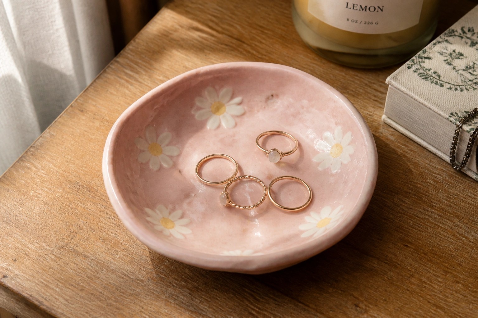 Pink daisy-patterned bowl holding three gold rings on wooden table