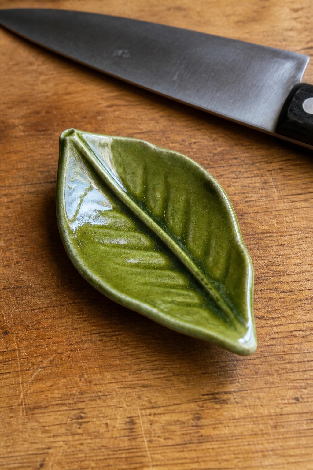 Green ceramic leaf dish beside knife on wooden cutting board