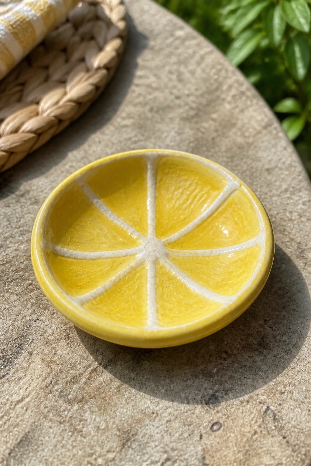 A small yellow ceramic dish shaped like a lemon slice with white dividing lines sits on a stone surface.