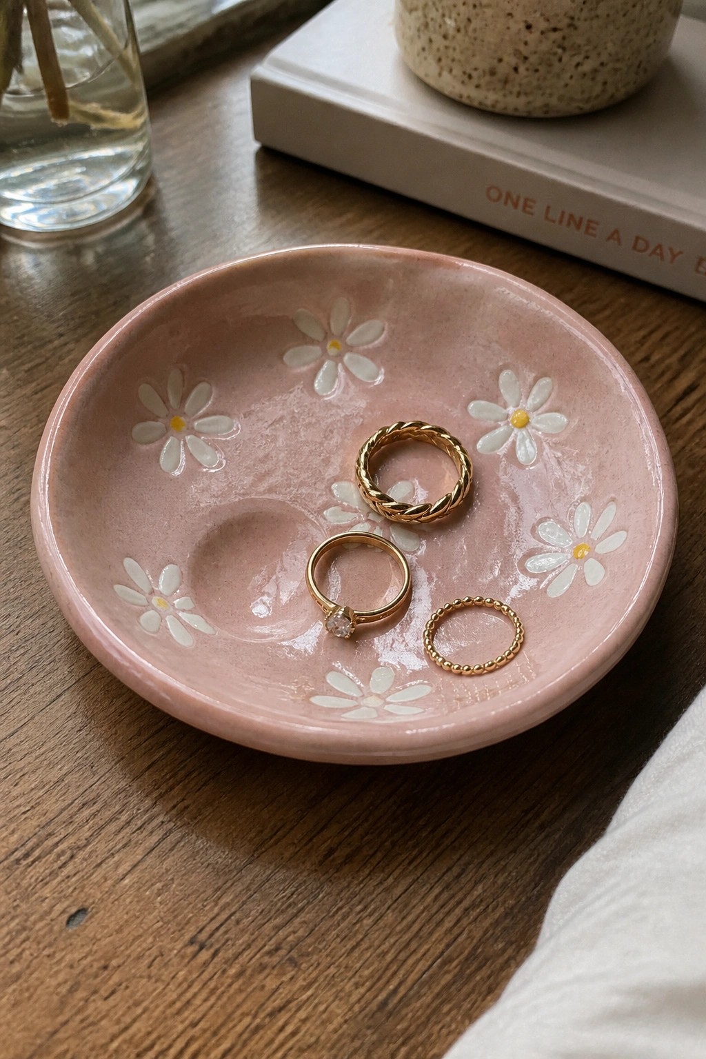 Pink daisy-patterned bowl holding three gold rings on wooden table