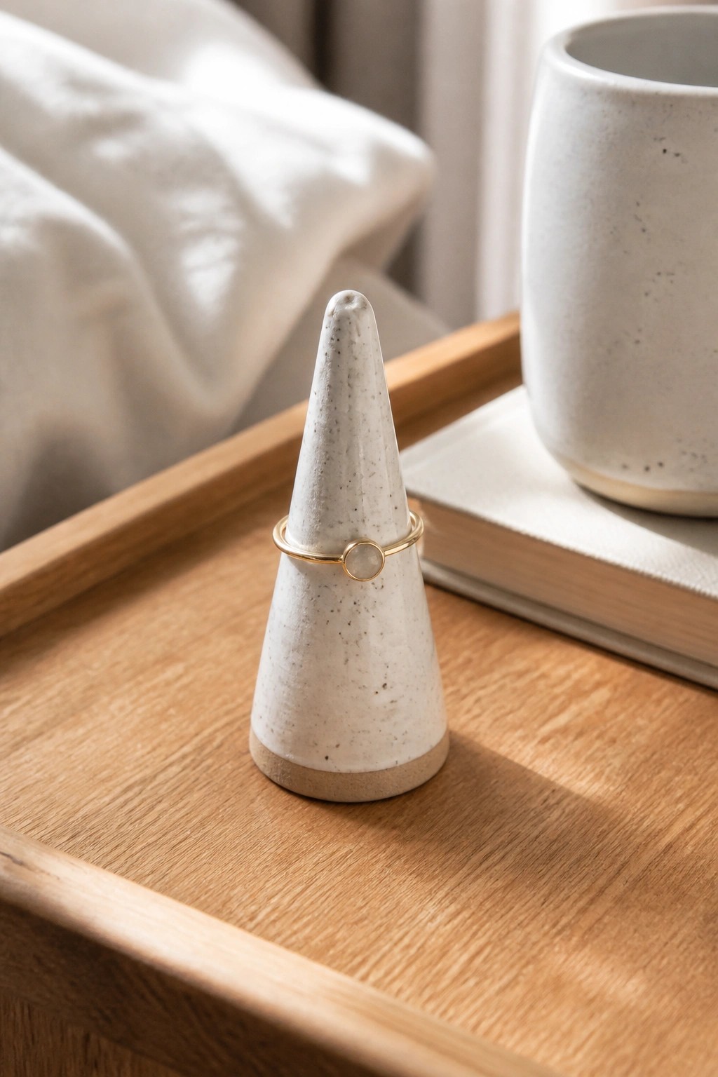 White ceramic cone ring holder with gold band on wooden tray beside mug