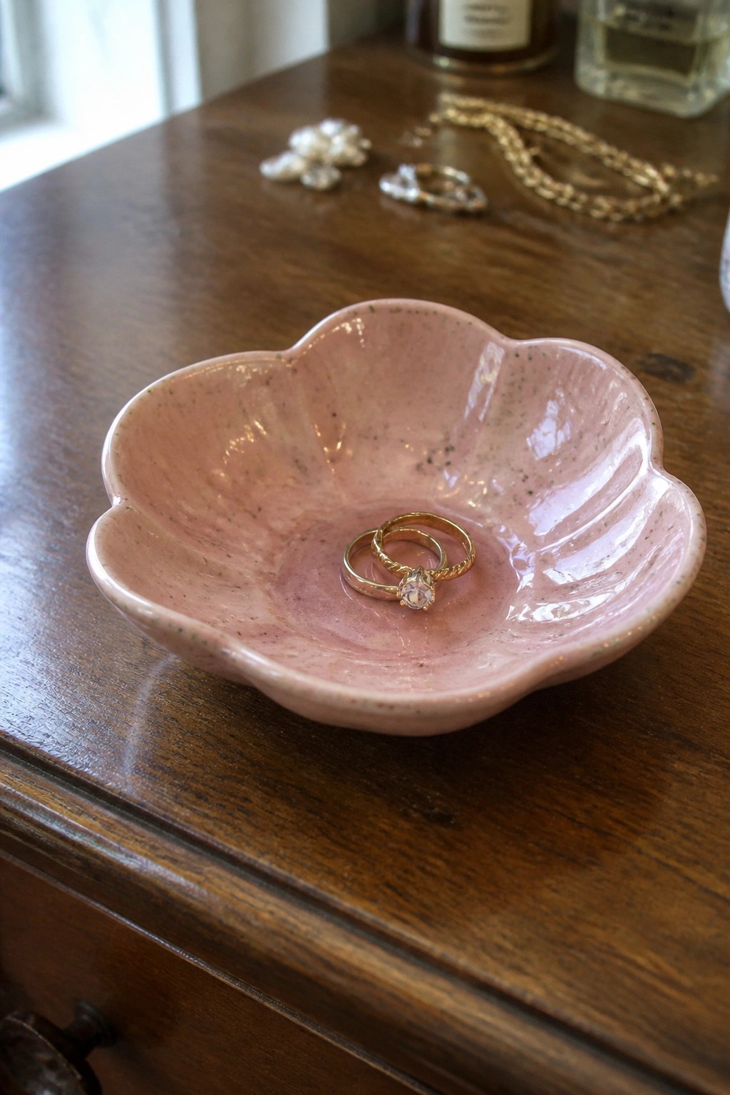 Pink flower-shaped bowl holding two gold rings on wooden table