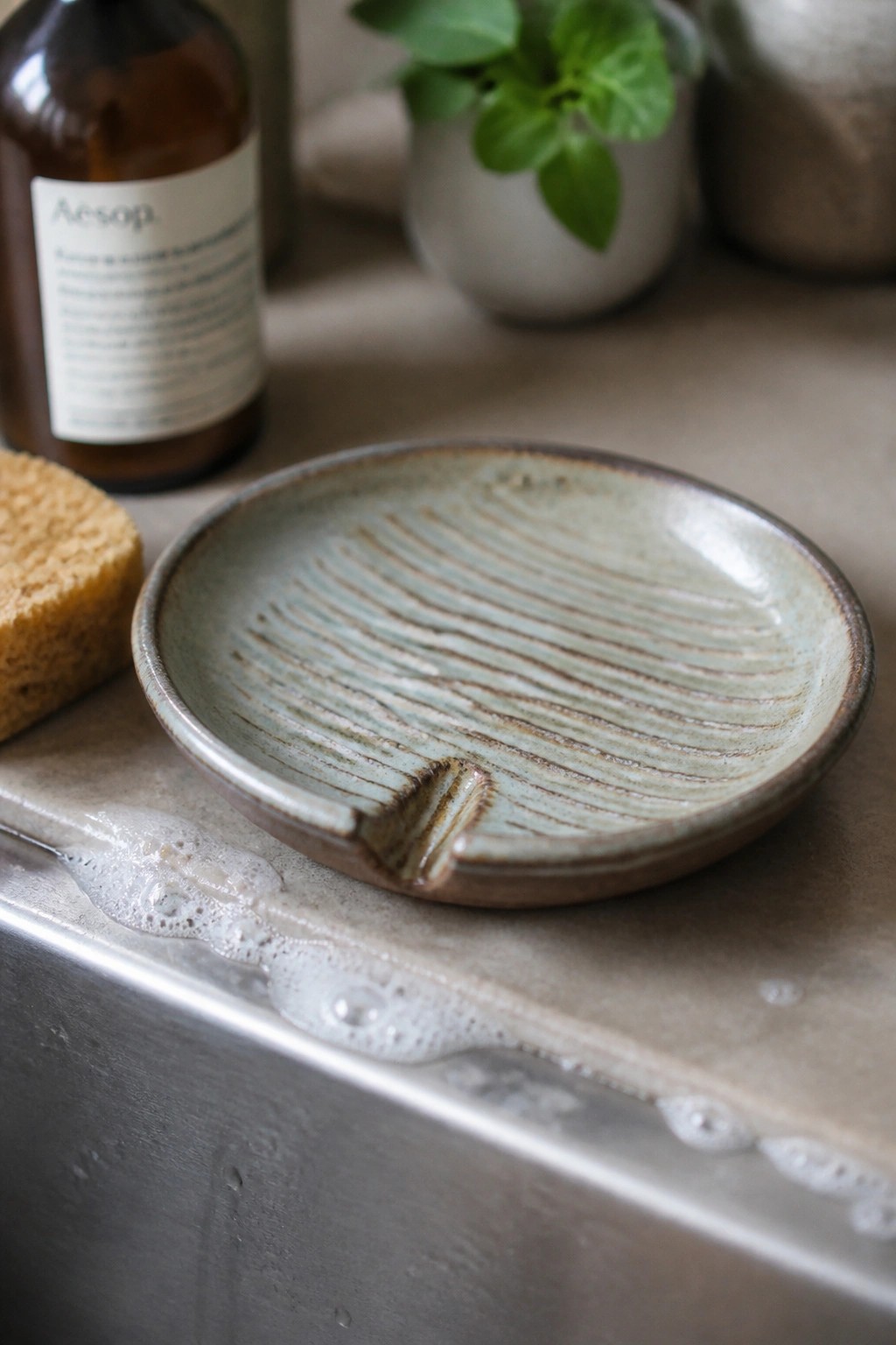 Ribbed ceramic soap dish with notch on wet sink beside sponge and foam