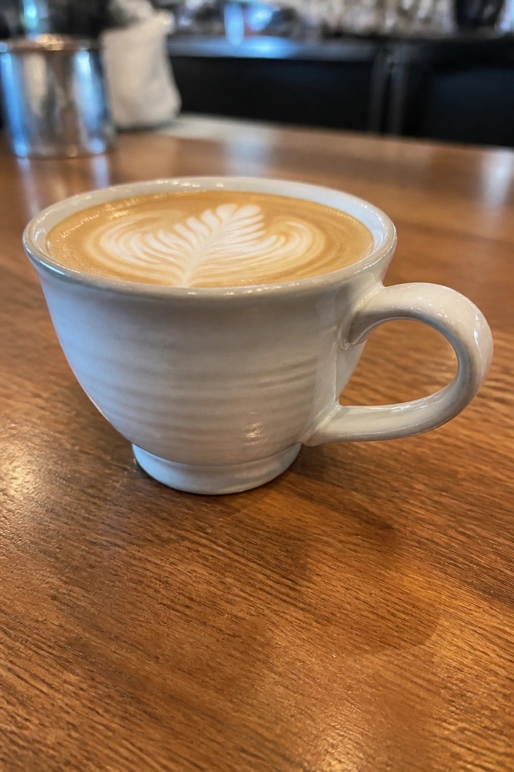 White ceramic mug with leaf latte art on wooden table