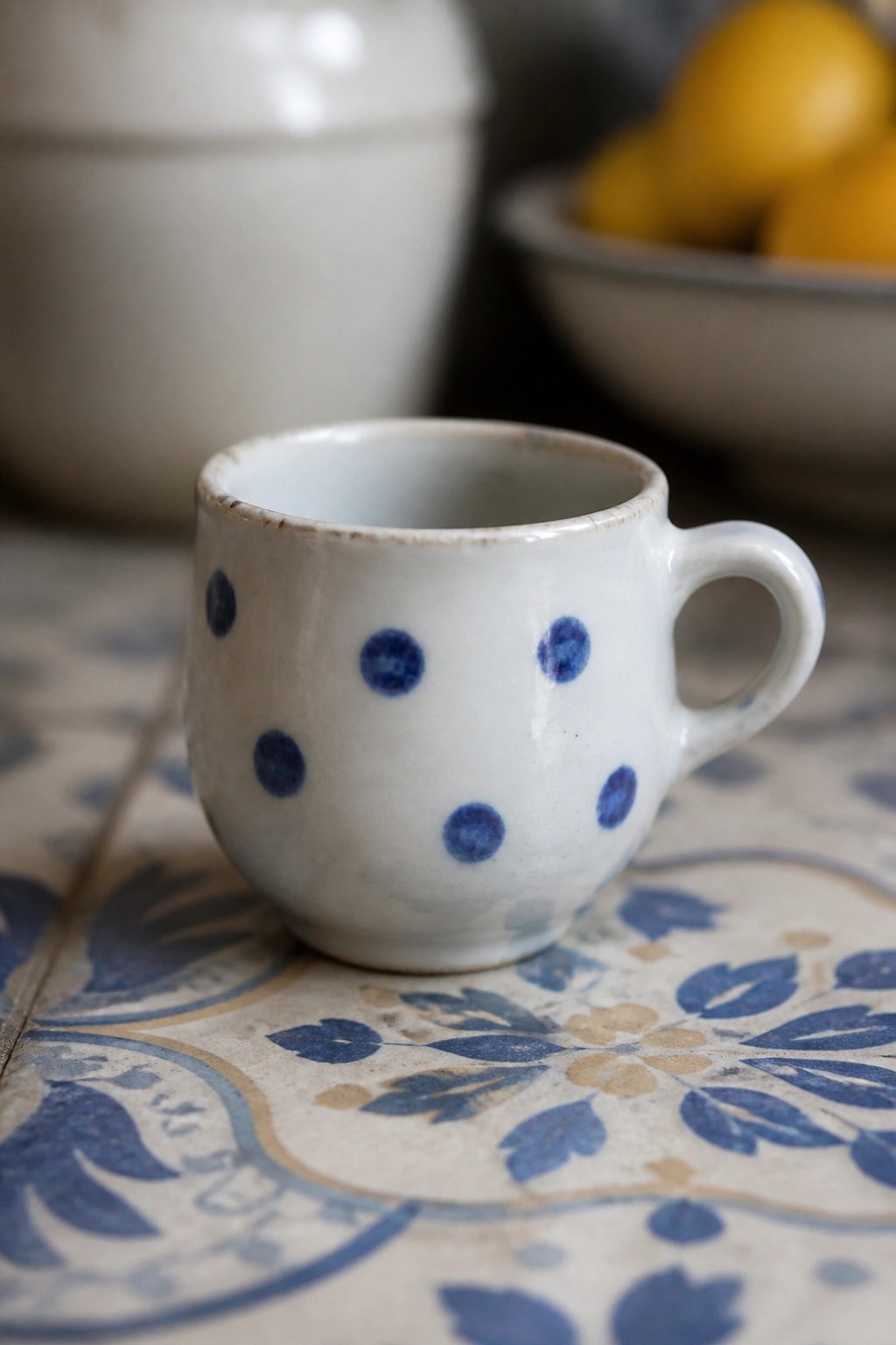 White ceramic cup with blue polka dots on patterned tile surface.