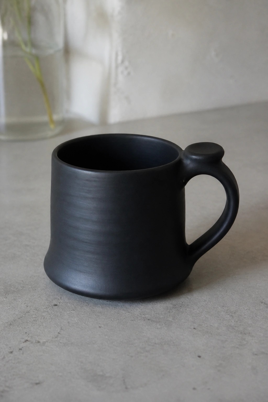 Matte black ceramic mug with knobbed handle on gray countertop