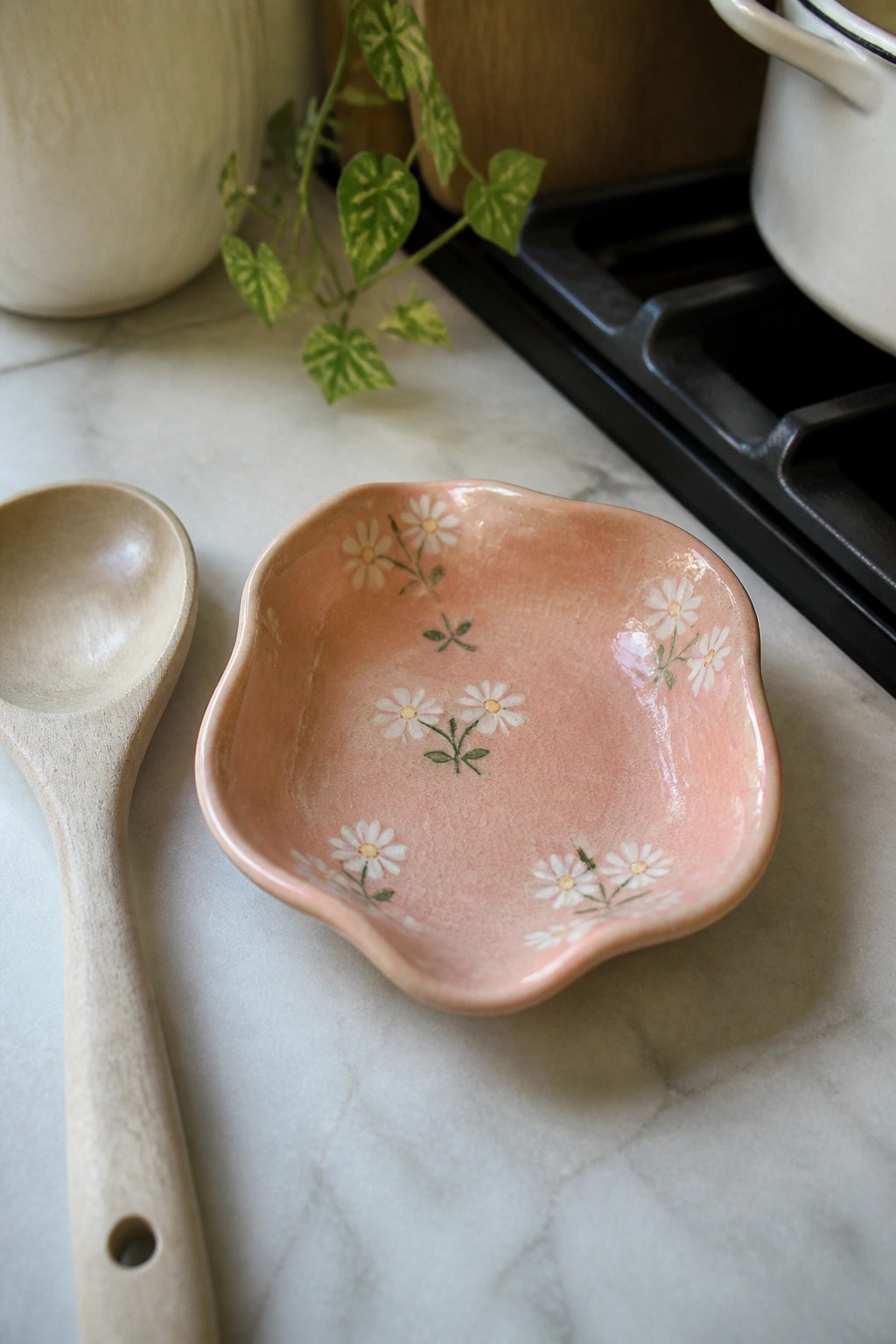 Pink ceramic bowl with white daisies beside wooden spoon on marble counter