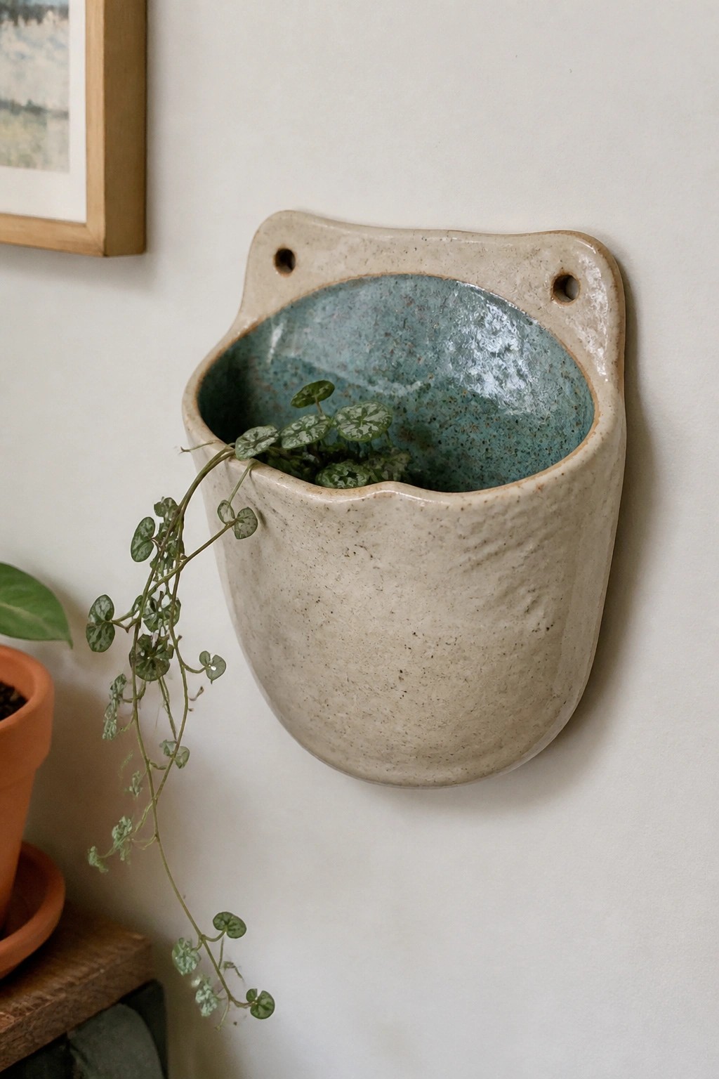 Beige ceramic wall planter with blue-green glaze and trailing green vine plant