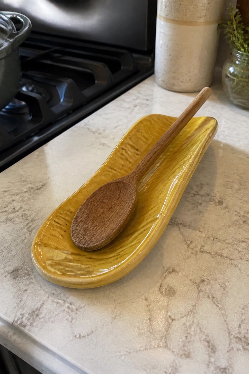 Wooden spoon resting in glossy yellow ceramic dish on marble countertop